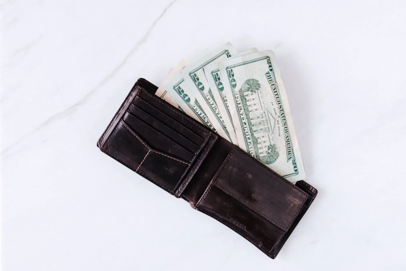 No copyright restriction An open brown wallet with United States twenty-dollar bills on a marble surface.