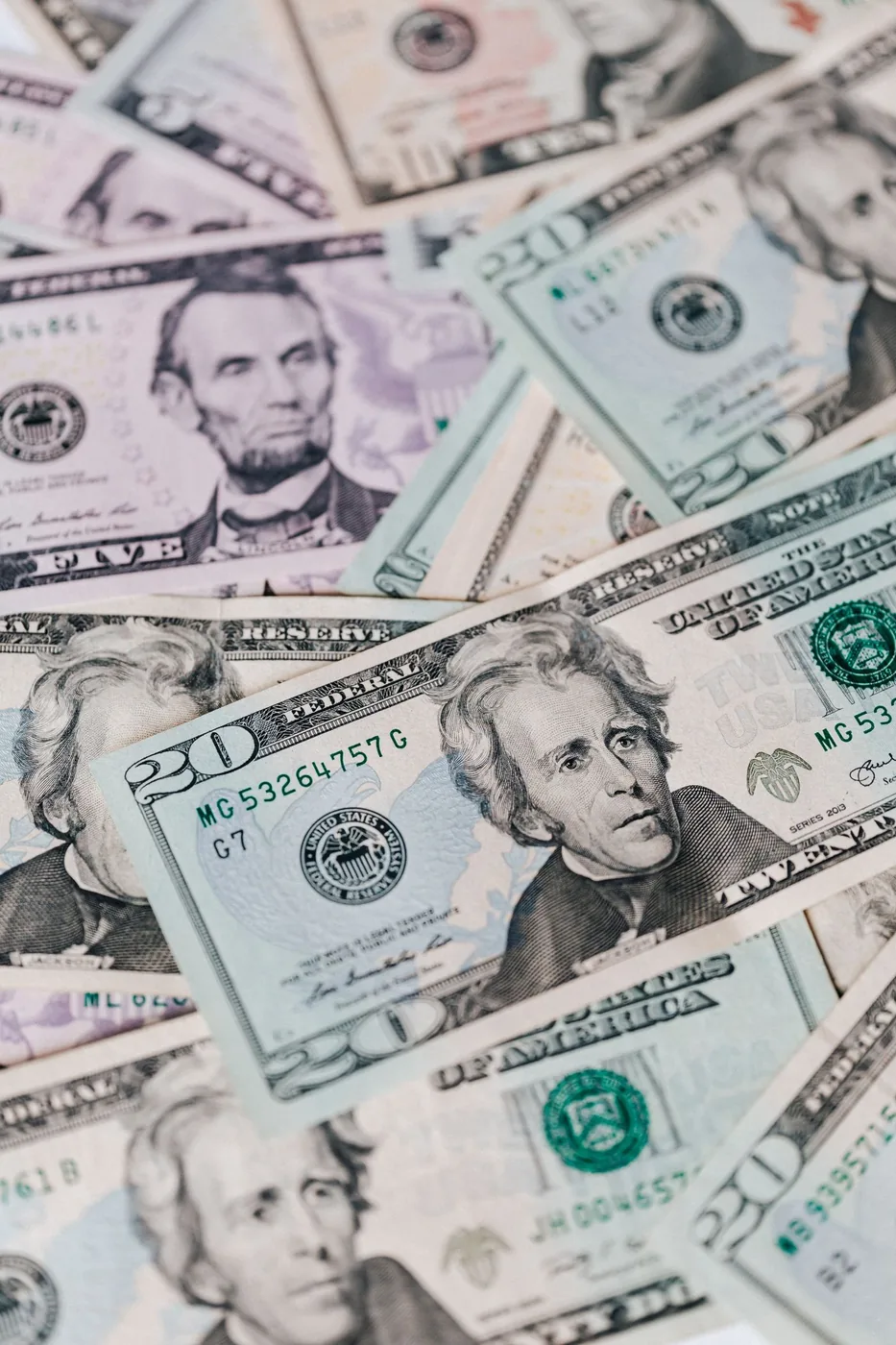 A scattered pile of United States five-dollar and twenty-dollar bills.