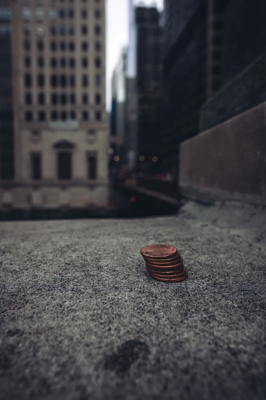 A small stack of pennies on a stone ledge with city buildings behind them.